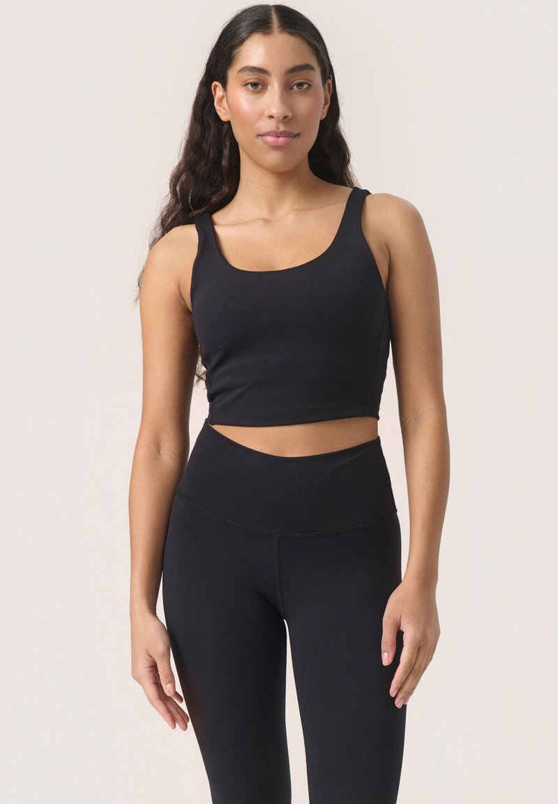Top croppato nero con spalline larghe, abbinato a leggings neri a vita alta. Texture liscia e design aderente, che crea un aspetto snello.