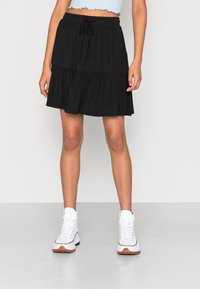 Svart lagerkjol med elastisk midjeband och dragsko. Tillverkad av mjukt tyg, har den en avslappnad design och når till mitten av låret.