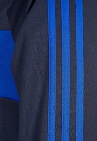 Marinblå atletisk tyg med ett blått randmönster bestående av tre parallella linjer. Texturen är slät med en lätt lyster.