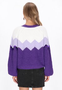 Sweter robiony na drutach z wzorem w zygzaku w odcieniach bieli, lawendy i fioletu. Ma teksturowane wykończenie i bufiaste rękawy, z dekoracyjnymi akcentami.