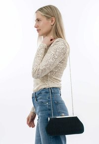 Borsa a busta verde plissettata con accessori in argento e tracolla a catena, abbinata a un top con paillettes e a jeans blu a vita alta.