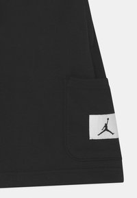Svarta bomullsshorts har en sid ficka med en vit etikett som visar en svart Jumpman-logotyp. Slät textur och standard atletisk design.