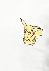 Κίτρινος χαρακτήρας κινουμένων σχεδίων με κόκκινα μάγουλα, αυτιά με μαύρα άκρα και ουρά σε σχήμα ζιγκ-ζαγκ, που χαμογελά και κάθεται σε λευκό υφασμάτινο φόντο.