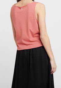 Koralfarvet tanktop med løs pasform, rund halsudskæring og blødt stof. Kombineret med et flydende sort nederdel, der fremhæver et lagdelt look.