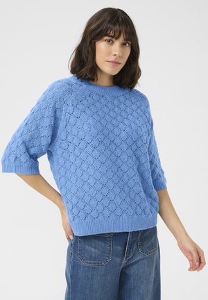 Light blue knitted sweater featuring a textured, wave pattern, short wide sleeves, and a ribbed hem. Paired with high-waisted jeans.