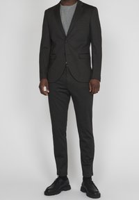 Mörkgrå skräddarsydd kostym med matchande byxor, strukturerat material, slim fit, blazer med en knapp, kombinerad med grå T-shirt och svarta skor.