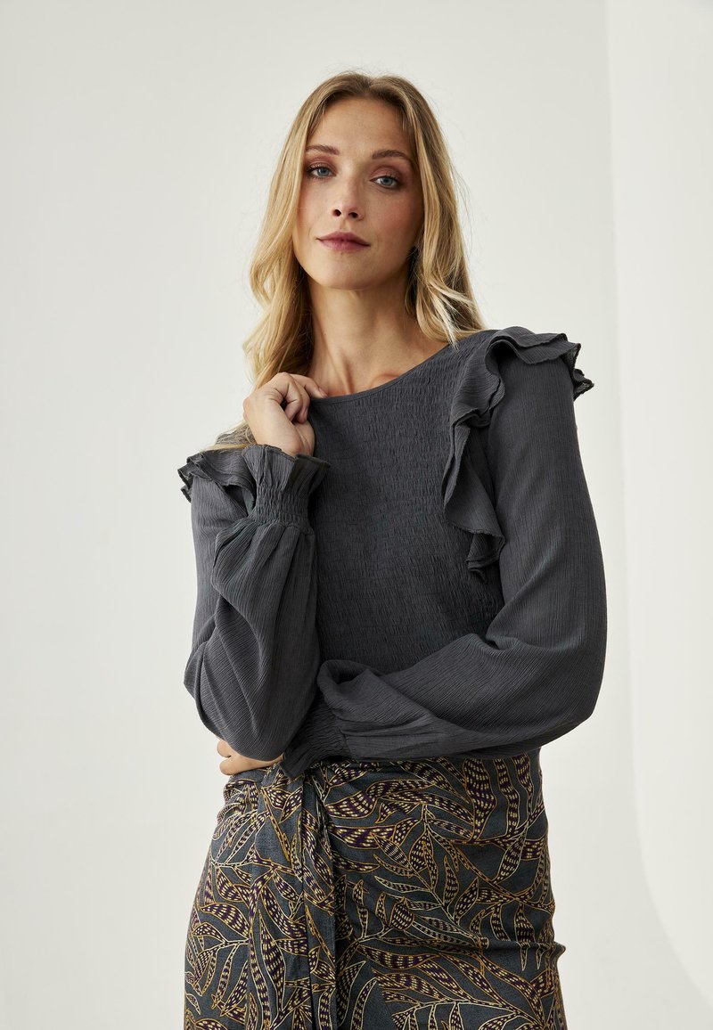 Blusa gris de manga larga con detalles en los hombros con volantes, de tejido texturizado, acompañada de una falda estampada con diseños de hojas en azul y dorado.