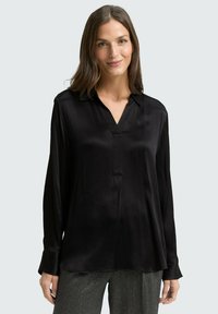 Blouse en satin noir avec un décolleté en V, des manches longues et une coupe décontractée. Présente une texture subtile et un détail à l'avant sans boutons.