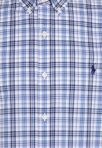 Blaues, schwarzes und weißes kariertes Hemd mit Knöpfen, Kragen und einem dunkelblauen, gestickten Polo-Spieler-Logo auf der rechten Seite.