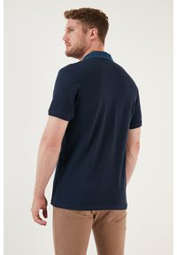 Námorně modrá polo košile s krátkým rukávem a denimu akcentem na límci. Hladký bavlněný materiál, přiléhavý design a jednoduchá zadní část bez dalšího vzoru.