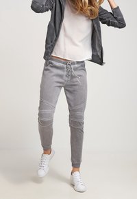 Pantalons de jogging gris avec une texture douce, dotés d'une taille avec cordon, de poignets côtelés et de détails de couture angulaires. Associés à des baskets blanches.