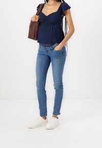 Top peplum de manga corta en azul oscuro, con detalle de escote fruncido, combinado con jeans ajustados en azul claro y zapatillas blancas. Bolsa de hombro marrón.