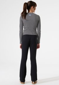 Gestreepte top met lange mouwen en een ronde halslijn, gecombineerd met zwarte flared broek. De top heeft blauwe borduursels aan de achterkant.