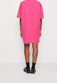 Lyhyt vaaleanpunainen mekko, jossa on löysä malli, pyöreä pääntie ja lyhyet hihat, yhdistettynä mustiin sukkiin ja kiiltäviin mustiin kenkiin.