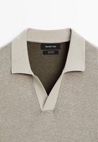 Maglione polo in cotone beige con un design a maglia testurizzata, colletto a V e finitura liscia del colletto; etichetta del marchio visibile all'interno.