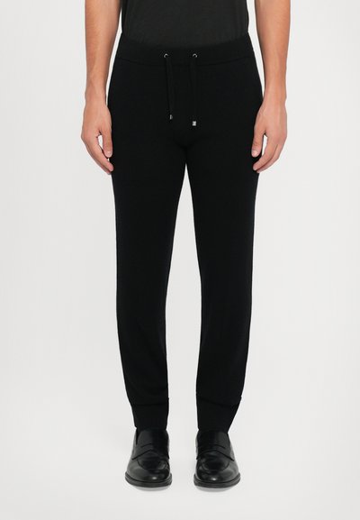 Sorte joggebukser med snøre i taljen og ribbede manchetter. Glat stofstruktur, slim-fit design, parret med sorte sko.