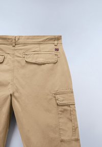 Beige cargo pants with flap pockets on back and thigh, featuring small Norwegian flag patch on right back pocket.