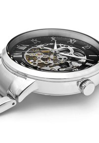 Montre mécanique en argent avec un cadran transparent. Présente des chiffres romains, des engrenages visibles et une couronne texturée. Détails noirs et dorés.