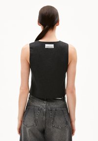 Schwarzes ärmelloses Top aus strukturiertem Stoff, mit geradem Schnitt und einem kleinen Etikett auf der Rückseite. Kombiniert mit verwaschenen Jeans.