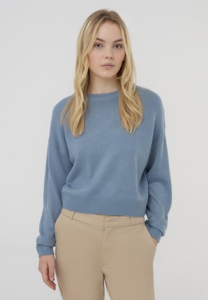 Maglione lavorato a maglia di colore azzurro chiaro con scollatura rotonda e polsini a coste, abbinato a pantaloni beige strutturati. Design semplice e dalla vestibilità rilassata.