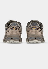 Grå och taupe löparskor med meshinlägg, förstärkt häl och texturerad sula. Har tydlig logotyp och ergonomiska designdetaljer.