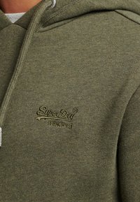 Sudadera verde oliva hecha de tela suave, con un bolsillo canguro en la parte delantera y un logo bordado de "Superdry" en el pecho.
