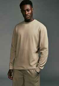Beige langwerpig shirt met lange mouwen van textuur katoen, met een ronde hals en ribgebreide manchetten, gecombineerd met bijpassende beige broek.