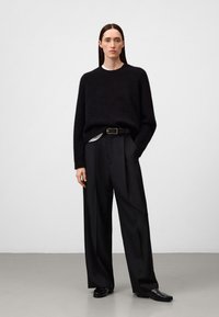 Schwarzer, flauschiger Wollpullover kombiniert mit hochgeschnittenen, weit geschnittenen schwarzen Hosen. Minimalistisches Design, subtile Eleganz und klassisches schwarzes Gürtel-Detail.