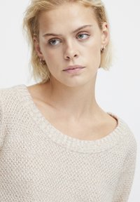 Beige gestrickter Pullover mit einem breiten, gerippten Ausschnitt und strukturiertem Stoff. Leicht lockere Passform mit sichtbaren Nähdetails.