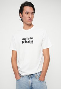 Biała bawełniana koszulka z okrągłym dekoltem, z wyraźnym czarnym napisem "calvin klein New York City" z przodu. Krótkie rękawy, luźny krój.