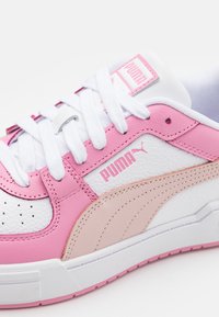 Rosa og hvit lær sneaker med hvite lisser, med en teksturert overflate, perforeringer og en rosa Puma-logo på siden.