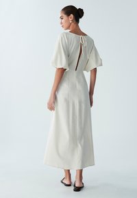 Linnen jurk in roomkleur met een losse pasvorm, korte pofmouwen en een striksluiting aan de achterkant. Het ontwerp heeft een lange, vloeiende silhouet.