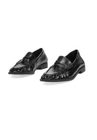 Mocasines de mujer de cuero negro con detalles de costura y tacones bajos, mostrados uno al lado del otro sobre un fondo blanco.