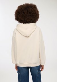 Felpa color crema con un ampio cappuccio, design morbido e polsini a costine, abbinata a pantaloni cargo in denim con tasche laterali.