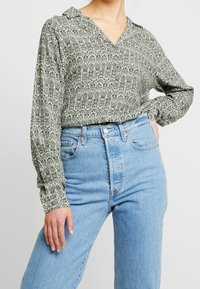 Grön mönstrad blus med krage, långa ärmar och v-ringning. Matchad med högmidjade ljusblå denimjeans. Mjuk tygtextur.