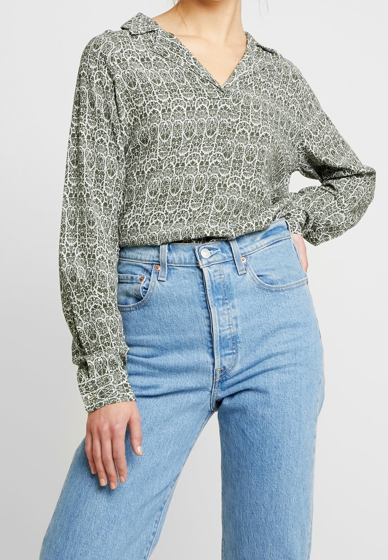 Grön mönstrad blus med krage, långa ärmar och v-ringning. Matchad med högmidjade ljusblå denimjeans. Mjuk tygtextur.