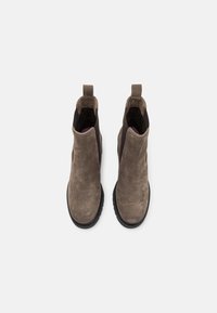 Botas de ante marrón hasta el tobillo con una textura suave, paneles laterales elásticos y lengüetas para facilitar el uso. Suelas de goma negra con un acabado texturizado.