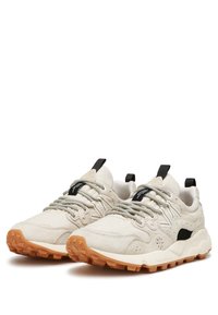 Beige sneakers med en texturerad ovandel, svarta accenter och tjocka gummisulor. Har en vadderad kant och elastiska snören för en säker passform.