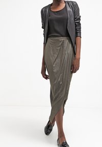 Metallisk grön pennkjol med draperad design, kombinerad med en svart topp och en figurnära läderjacka. Svarta lackpumps fulländar outfiten.