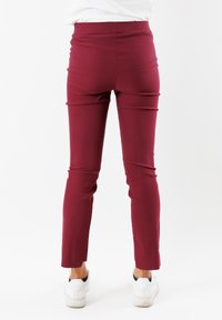 Pantaloni slim-fit bordeaux con una texture liscia e taglio alla caviglia, abbinati a sneaker bianche per un contrasto.
