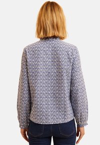 Blusa floreale blu con maniche lunghe, polsini arricciati e scollo rotondo. Presenta un motivo floreale bianco su un tessuto testurizzato.