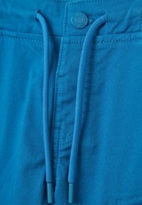 Pantalones cortos de tela azul con una textura suave, que presentan un cordón en la cintura y un cierre de botón. La costura es visible a lo largo de los bordes.