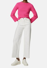 Pull rose en tricot avec un col rond et des manches longues, associé à un jean blanc à jambes larges et des baskets blanches.