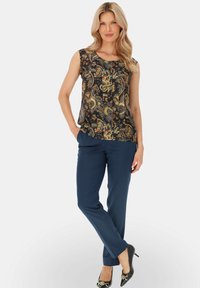 Czarna top bez rękawów z wzorem paisley, połączony z granatowymi spodniami. Modelka nosząca czarne szpilki z srebrnymi akcentami.