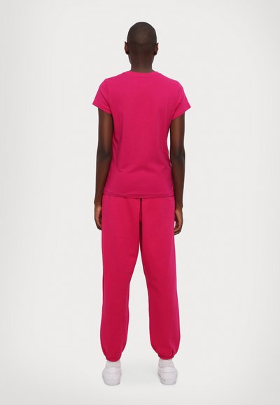 T-shirt de algodão rosa e calças de fato combinando, corte descontraído, com punhos elásticos nas calças e decote redondo na parte de cima. Ténis brancos completam o visual.