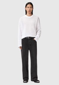 Hvid tekstureret sweater med lange ærmer, parret med højtaljede sorte vidde bukser og sorte sko med hvide accenter. Sort bælte inkluderet.