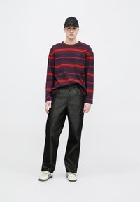 Μακρυμάνικη μπλε ναυτική και κόκκινη ριγέ μπλούζα σε συνδυασμό με μαύρο τζιν φαρδιάς γραμμής και λευκά αθλητικά παπούτσια, ολοκληρωμένη με μαύρο καπέλο με λογότυπο.