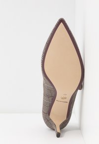 Chaussure à talon aigu avec un dessus en tissu à carreaux reposant sur le côté de la semelle contre une surface blanche à coins.