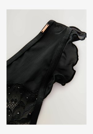 Melnas mežģīņu krūšturis ar acīm līdzīgiem paneļiem, viļņotām malām un dekoratīvām pērlītēm. Ietver vara krāsas metāla birku ar zīmola nosaukumu.