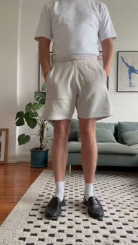 Shorts gris, à texture douce, arrivant au genou, avec une taille élastique, associés à des mocassins noirs et des chaussettes blanches, dans un salon domestique.